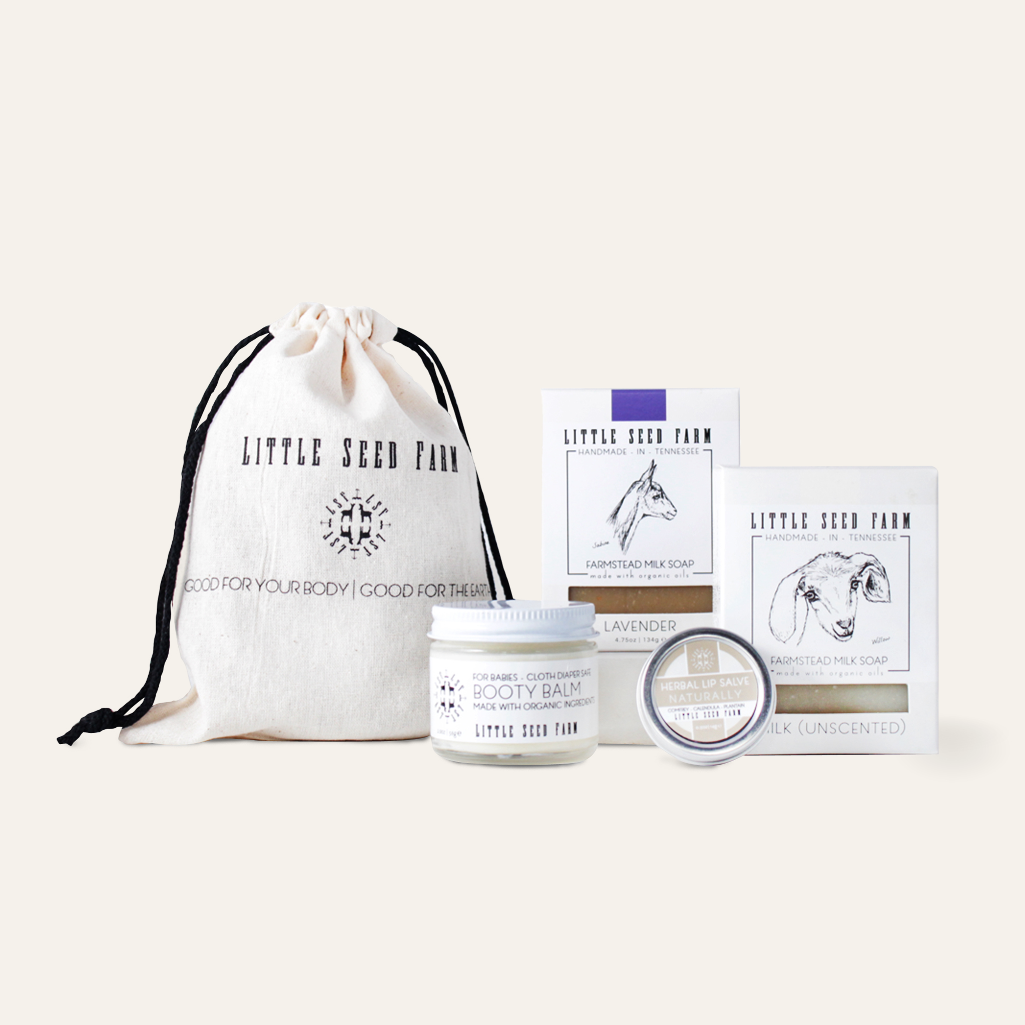 A neatly arranged Organic Baby Gift Set featuring Booty Balm for Babies, Naturally Herbal Lip Salve, Lavender Bar, and Milk Bar, all packaged in a reusable cotton pouch.