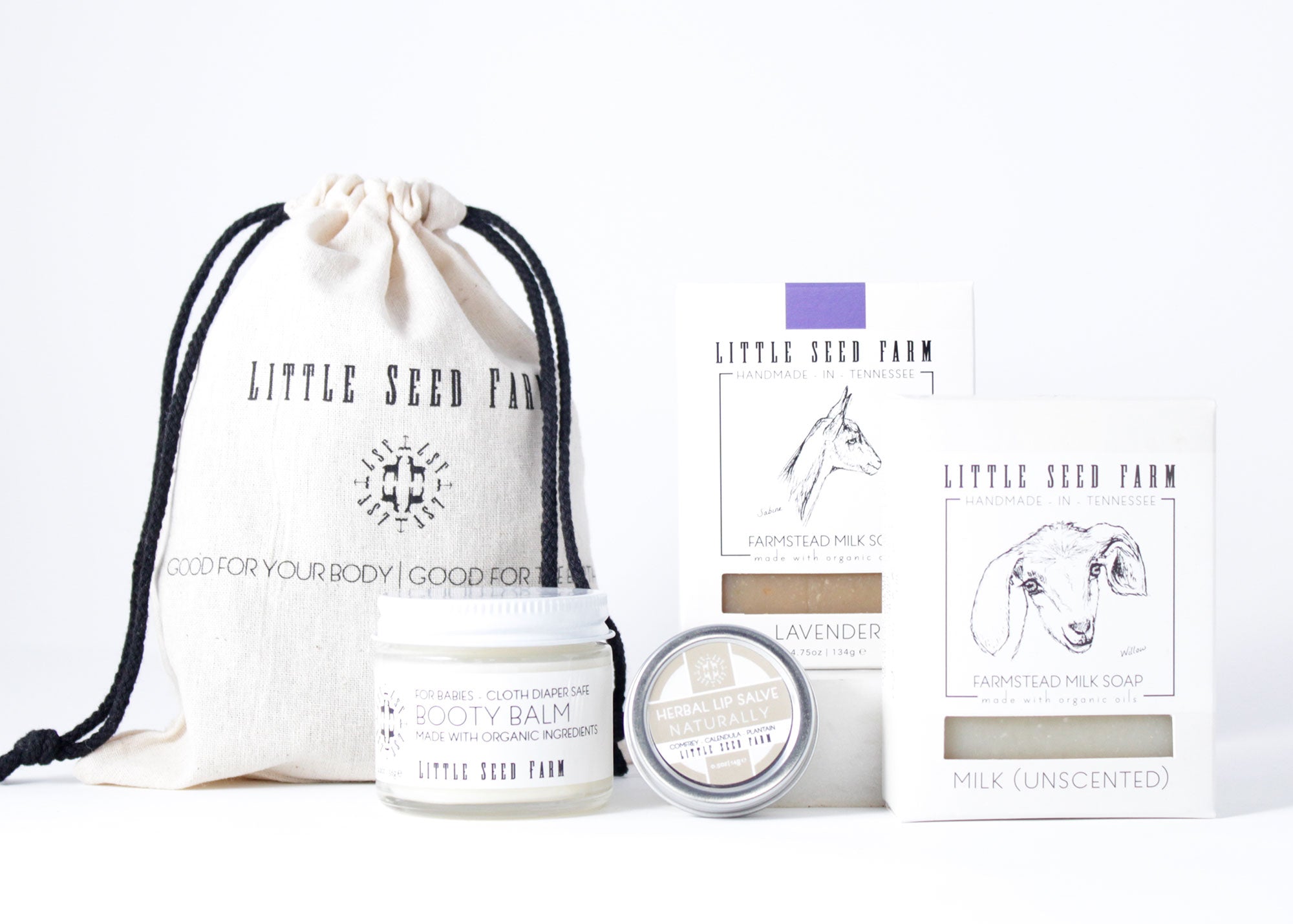 A neatly arranged Organic Baby Gift Set featuring Booty Balm for Babies, Naturally Herbal Lip Salve, Lavender Bar, and Milk Bar, all packaged in a reusable cotton pouch.