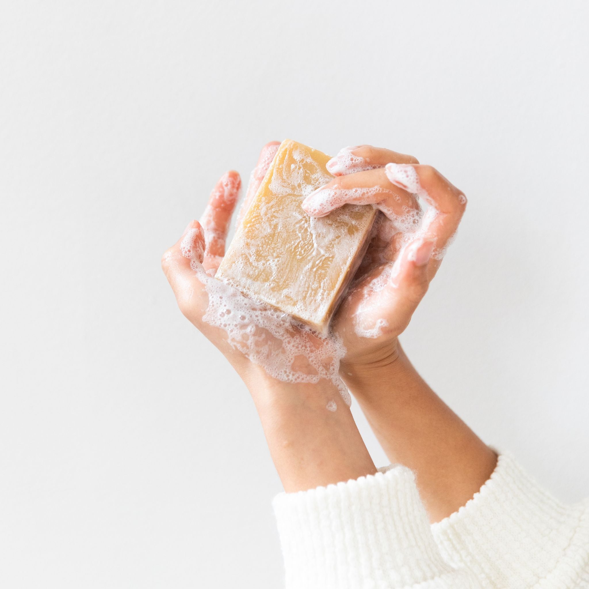 Hand holding Little Seed Farm’s lathered goat milk soap bar, showcasing rich suds and gentle cleansing formula.