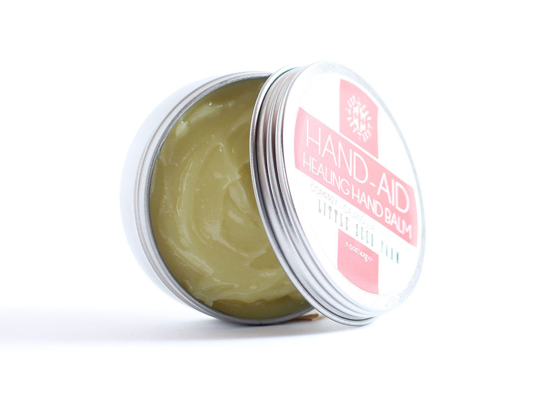 Open tin of Original Hand‑Aid Healing Hand Balm revealing dense, herb-rich formula for deeply moisturizing hardworking hands”—an organic healing blend beloved by nurses, farmers, and potters