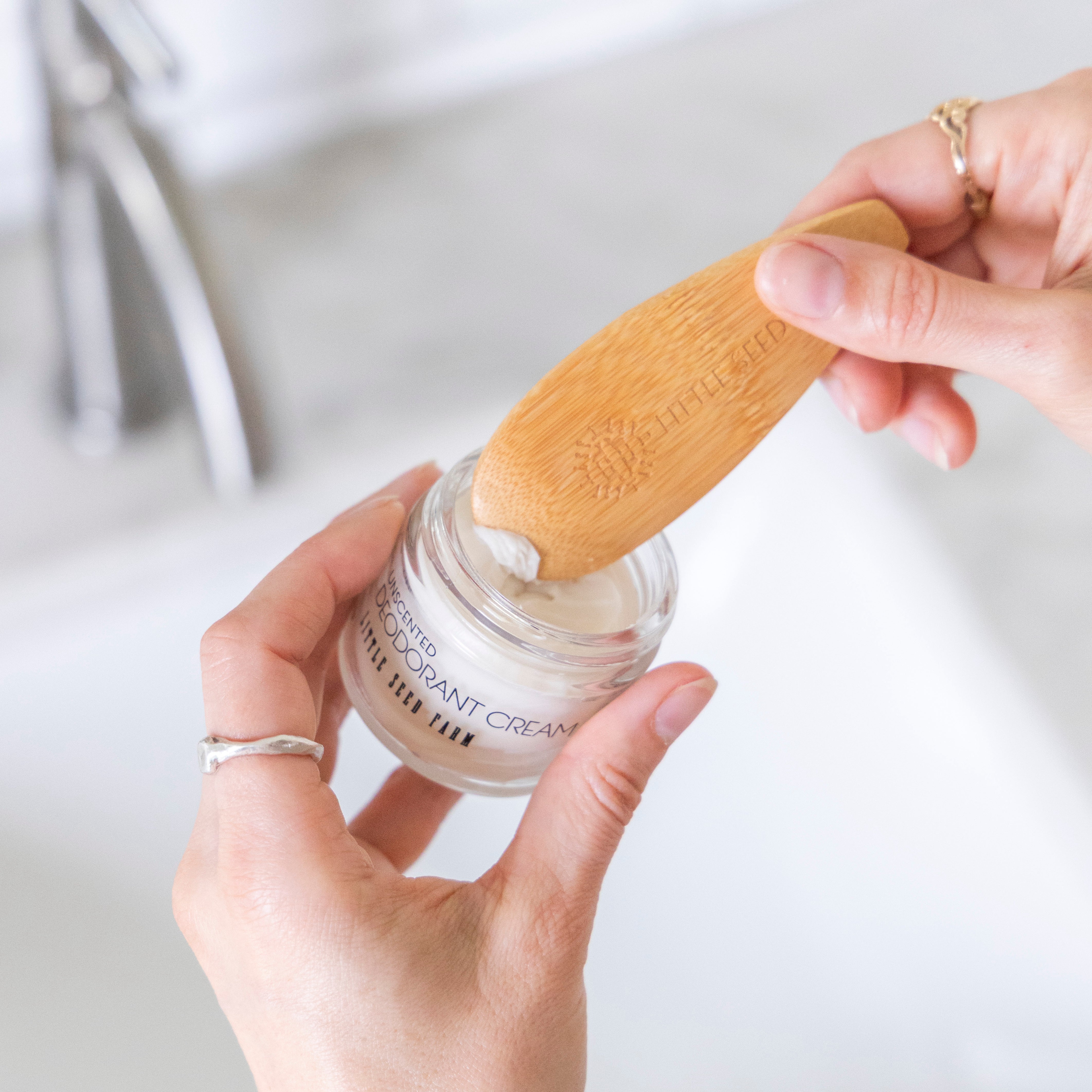 Person applying a deodorant cream with a wooden applicator on a light background