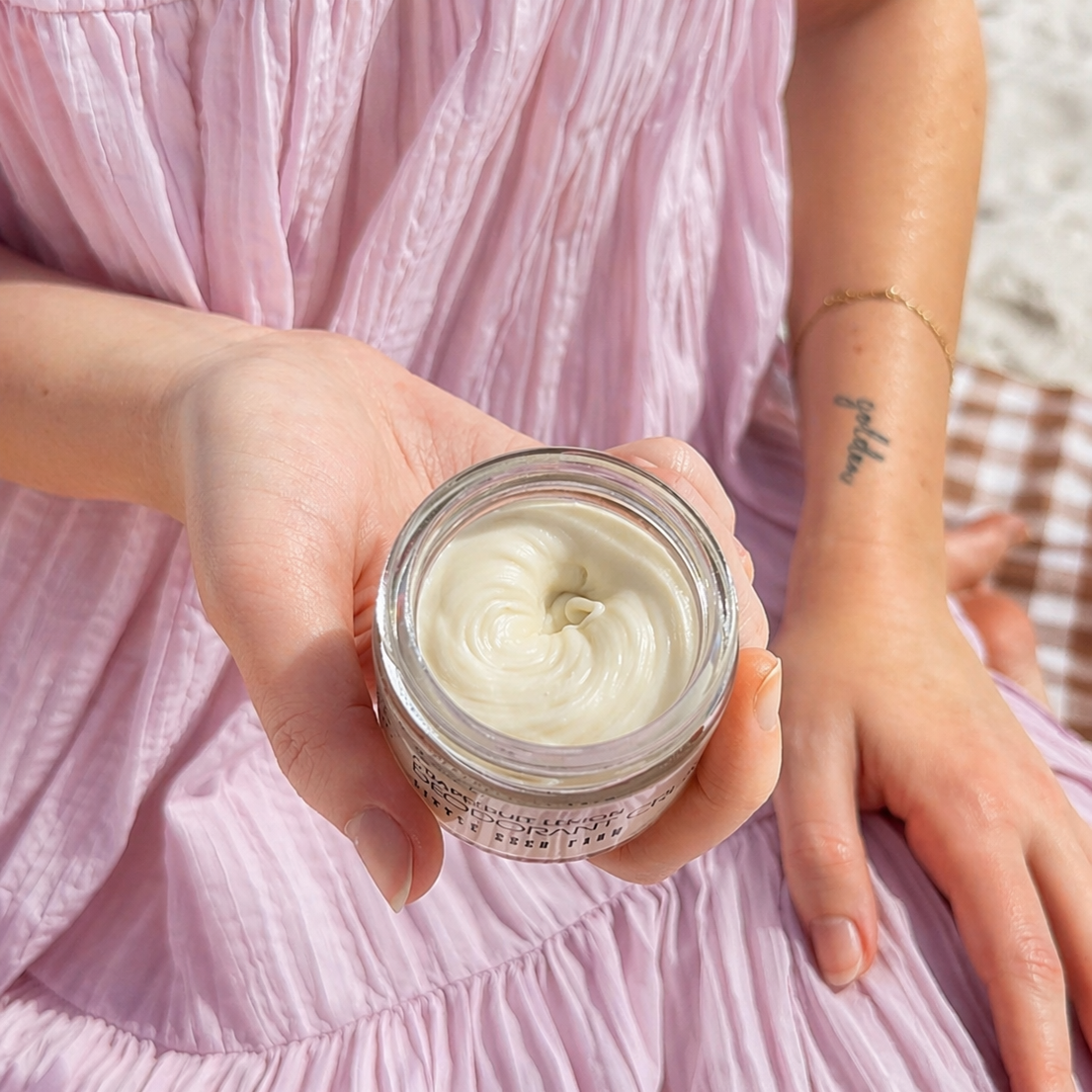 Person holding a jar of little seed farm deodorant cream with a pink dress in the background